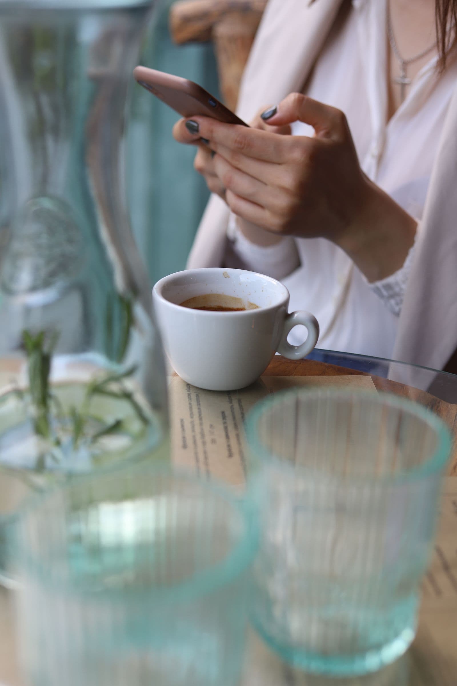 A hand holding a phone over a cafe table with coffee