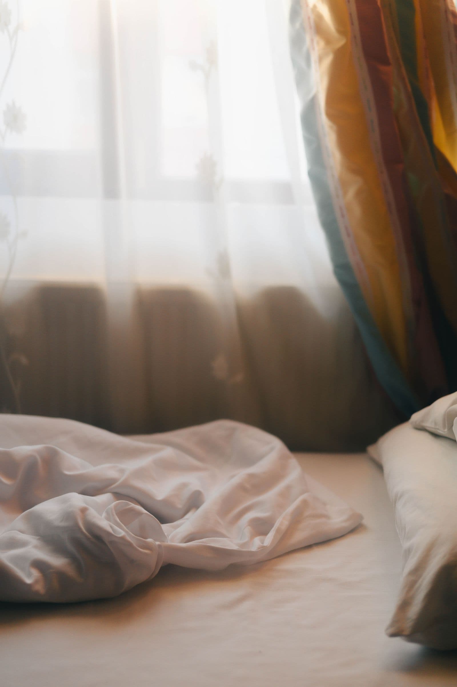 Soft morning light falling through curtains onto a bed
