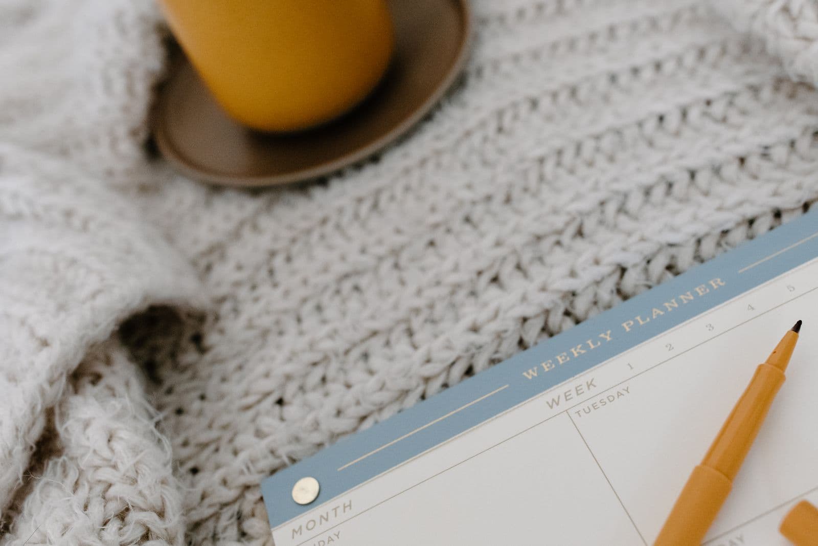 A weekly planner and warm drink resting on a knitted blanket